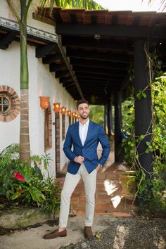 a man wearing a blue jacket and white pants standing in front of a building with palm trees