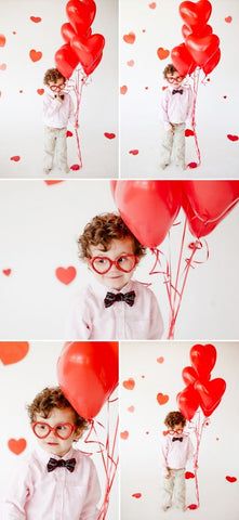 a little boy wearing glasses and bow tie holding red heart shaped balloons in front of his face