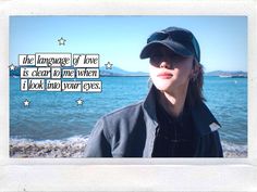 a woman standing in front of the ocean wearing a hat and sunglasses with words written on it