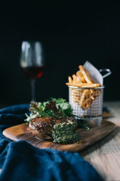 a wooden cutting board topped with steak and fries next to a glass of red wine