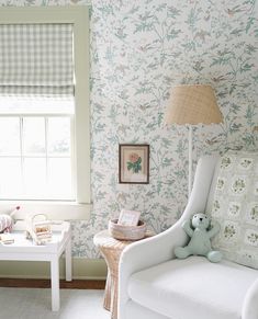 a white chair sitting next to a window in a room with floral wallpaper on the walls