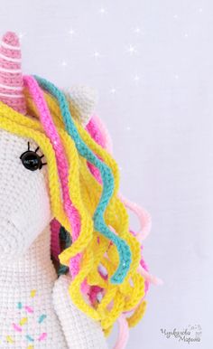 a crocheted stuffed unicorn with a pink, yellow, and blue mane on it's head