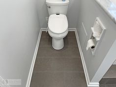 a white toilet sitting in a bathroom next to a roll of toilet paper on the wall