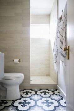 a white toilet sitting inside of a bathroom next to a walk in shower stall and tiled floor