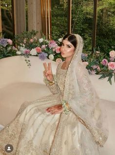 a woman in a wedding dress sitting on a couch with flowers around her and making the peace sign