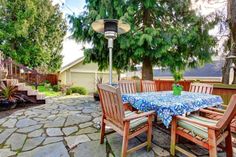 an outdoor table and chairs are set up on the stone patio with trees in the background