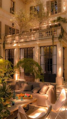 a living room filled with furniture next to a tall white building surrounded by greenery