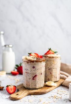 two jars filled with oatmeal and strawberries on top of a cutting board