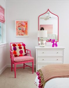 a white bedroom with pink accents and a mirror on the wall above the bed, along with a pink chair