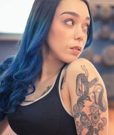 a woman with blue hair and tattoos on her arm looking off to the side,