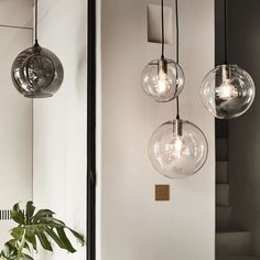 three glass globe lights hanging from the ceiling in a room with white walls and stairs