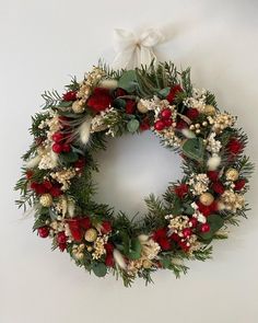 a christmas wreath hanging on the wall with red and white flowers, greenery and pine cones