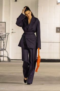 a woman is walking down the street with an orange purse in her hand and wearing a black suit