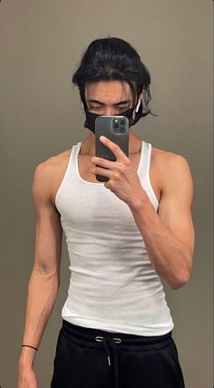 a man in white tank top taking a selfie with his cell phone while wearing black sweatpants