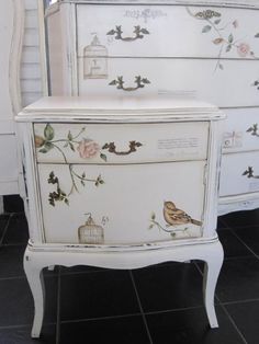 a white dresser sitting on top of a black tile floor next to a wall with flowers and birds painted on it