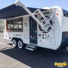 a white and blue camper parked in a parking lot next to a building with an awning