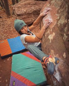 a woman climbing up the side of a large rock with colorful tarps on it