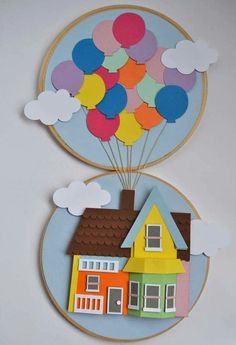 two paper houses with balloons floating over them on a white wall above a blue circle