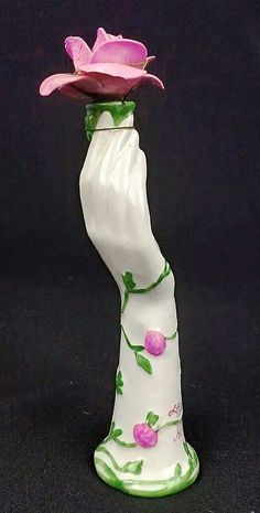 a white vase with a pink flower on it's top and green trim around the bottom