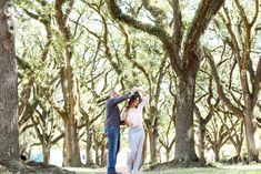 a man and woman dancing in the middle of a park with trees lining the sides