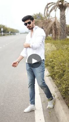 a man in white shirt and jeans standing on the side of a road next to palm trees