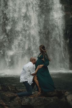 a pregnant couple standing in front of a waterfall