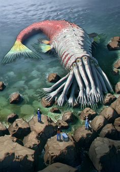 two people are standing in the water next to a giant fish that is floating over rocks