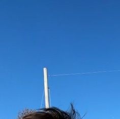 a woman is flying a kite in the blue sky with her hair blowing in the wind