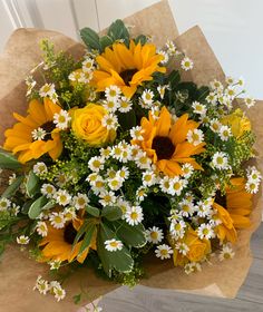 a bouquet of sunflowers and daisies on a brown paper bag with greenery