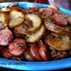 a blue plate filled with cooked potatoes and sausages on top of a wooden table