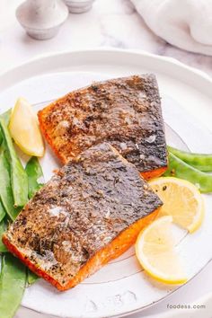 two pieces of fish on a plate with green beans and lemons next to it