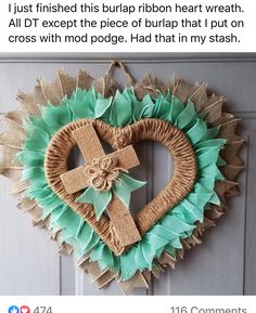 a heart shaped wreath with a cross hanging on the front door, decorated with burlap