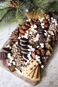 an assortment of cookies and marshmallows on a cutting board next to a pine tree