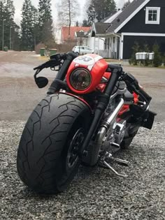 a red and black motorcycle parked on gravel next to a house with trees in the background