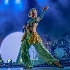 a woman is performing on stage with her arms in the air