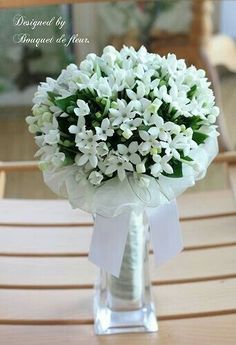 a bouquet of white flowers sitting on top of a wooden table next to a chair