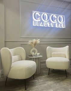 two white chairs sitting next to each other in front of a sign that says coco beauty bar