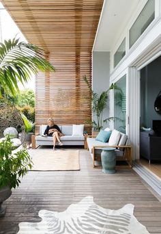 a person sitting on a couch in the middle of a room with plants and furniture