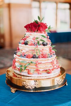 a multi layer cake with berries and flowers on top sits on a gold platter