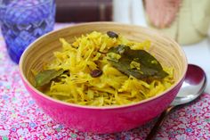 a pink bowl filled with yellow flowers and greens on top of a floral table cloth