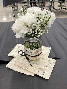 white flowers in a mason jar on top of music sheets