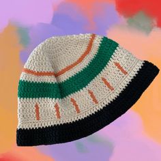 a crocheted beanie hat on top of a multicolored background with an orange, white, and green stripe