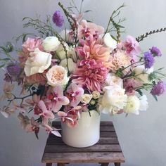 a white vase filled with lots of pink and white flowers on top of a wooden table