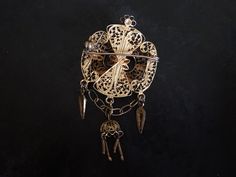 "This handsome, flickering brooch features detailed filigree and cannetille work. The brooch is quite dimensional with raised and dangling ornament. It was probably made in Portugal or Spain. The security clasp works just fine. The brooch is in good shape with some surface wear to the gilding. It is 6.7cm (2 5/8\")long X 3.2cm (1 1/4\")wide. It weighs 10g." Ornate Gold Locket Brooches, Ornate Wedding Brooch With Intricate Design, Ornate Wedding Brooches With Intricate Design, Antique Pendant Brooch With Intricate Design, Antique Brooch With Intricate Pendant Design, Antique Yellow Gold Filigree Brooches, Victorian Gold Pendant Brooches, Victorian Gold Brooch With Intricate Design, Victorian Gold Brooches With Intricate Design