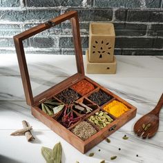 a wooden box filled with spices next to a spoon and spice grinder on a table