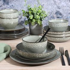 a table set for four with plates and silverware on it, next to a potted plant