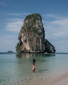 a woman wading in shallow water near an island with a rock outcropping