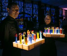 two people standing next to each other holding trays with different colored lighters on them