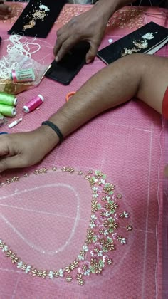 someone is making something out of beads on a pink table cloth with scissors and other crafting supplies