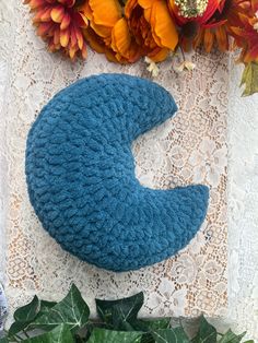 a blue knitted crescent sits on a lace tablecloth next to flowers and leaves